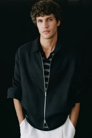 Model Francisco Henriques wearing a dark zip jacket and striped shirt against a black background for Massimo Dutti