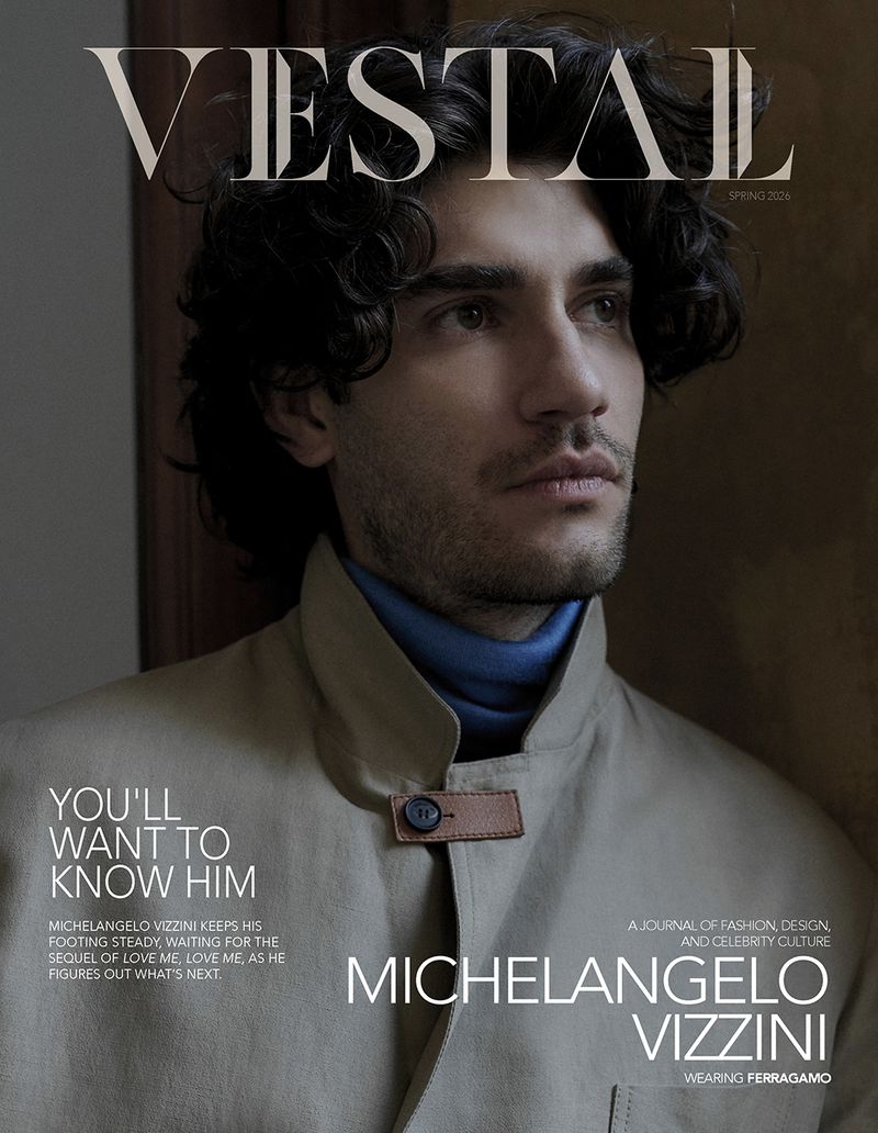 Portrait of a man wearing a beige coat with a blue turtleneck collar against a dark interior background for Vestal Magazine.