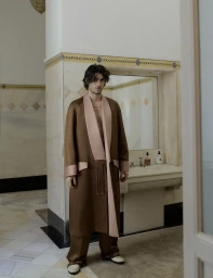 Man wearing a brown patterned robe with pink lapels standing in a marble-tiled bathroom for Vestal Magazine editorial