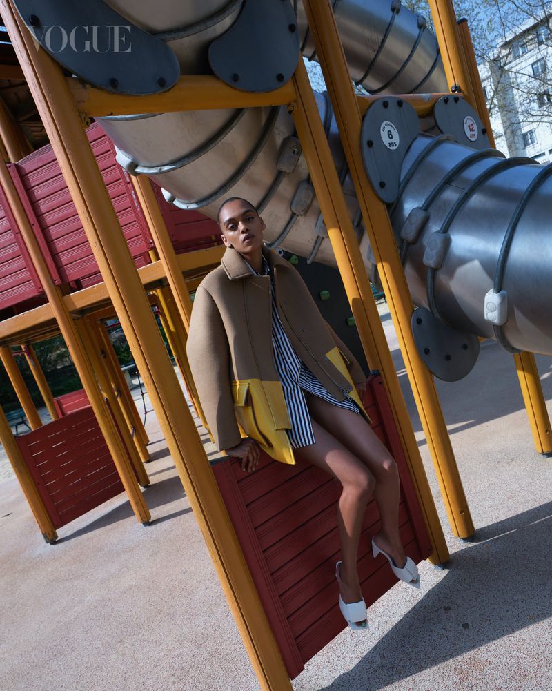 Model seated on playground structure wearing a beige jacket and striped shirt photographed by Jumbo Tsui.