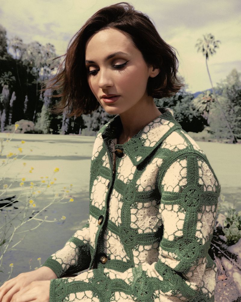 Maude Apatow wearing a patterned green and white jacket outdoors by a park water feature for Who What Wear