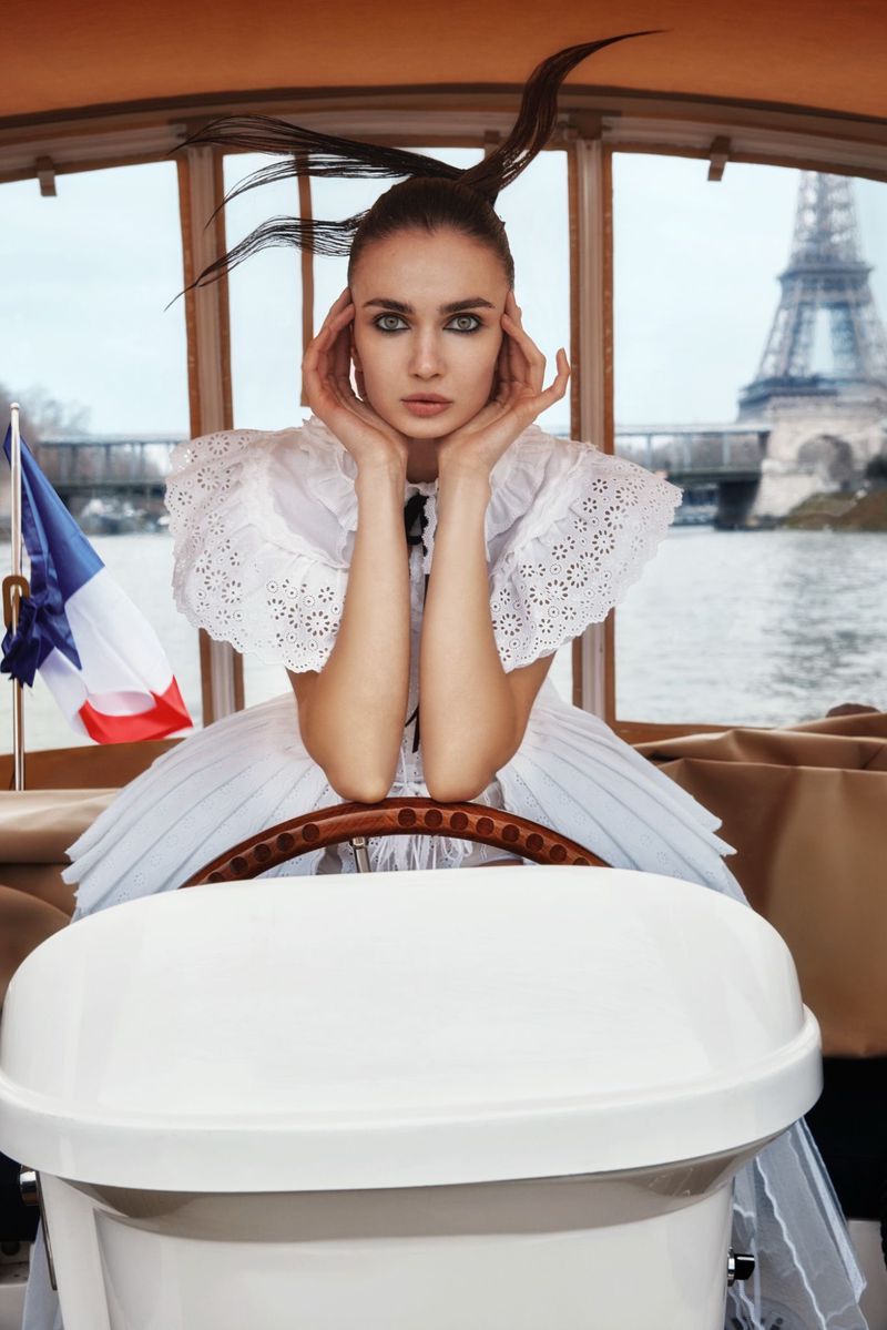 Woman in white dress poses in boat with Eiffel Tower view, Paris, France. She is holding her face with both hands.