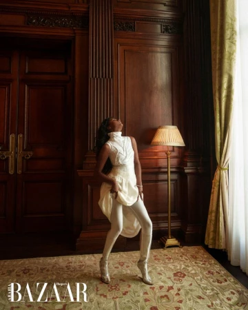 Simone Ashley wearing a white turtleneck and trousers in a wood-paneled room for Harper's Bazaar Arabia