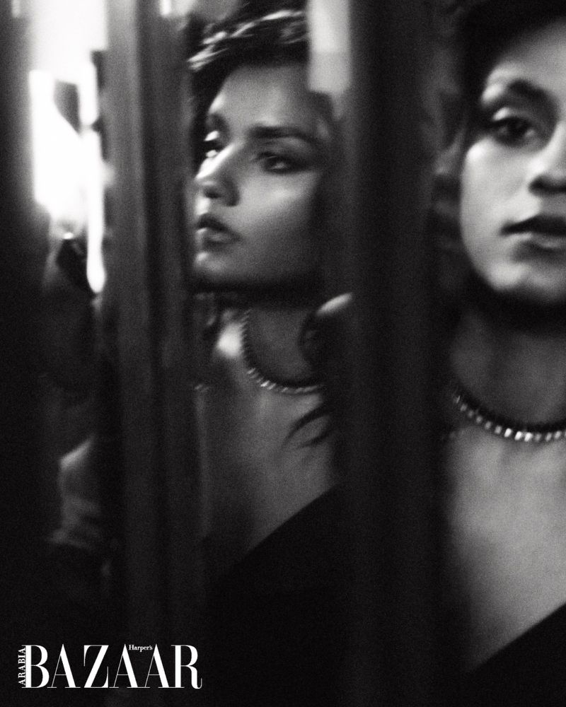 Black and white portrait of Simone Ashley wearing a necklace, reflected through vertical bars for Harper's Bazaar Arabia