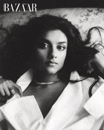 Portrait of Simone Ashley in a white collared shirt with a diamond choker necklace against a patterned backdrop for Harper's Bazaar Arabia