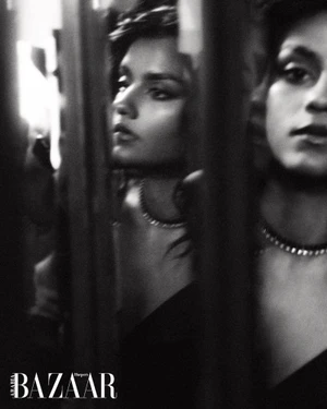 Black and white portrait of Simone Ashley wearing a necklace, reflected through vertical bars for Harper's Bazaar Arabia
