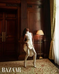 Simone Ashley wearing a white turtleneck and trousers in a wood-paneled room for Harper's Bazaar Arabia