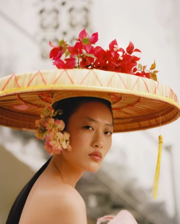 Model wearing a wide conical hat adorned with bright red flowers for Glass Magazine China ISLAND editorial by Mario Wang