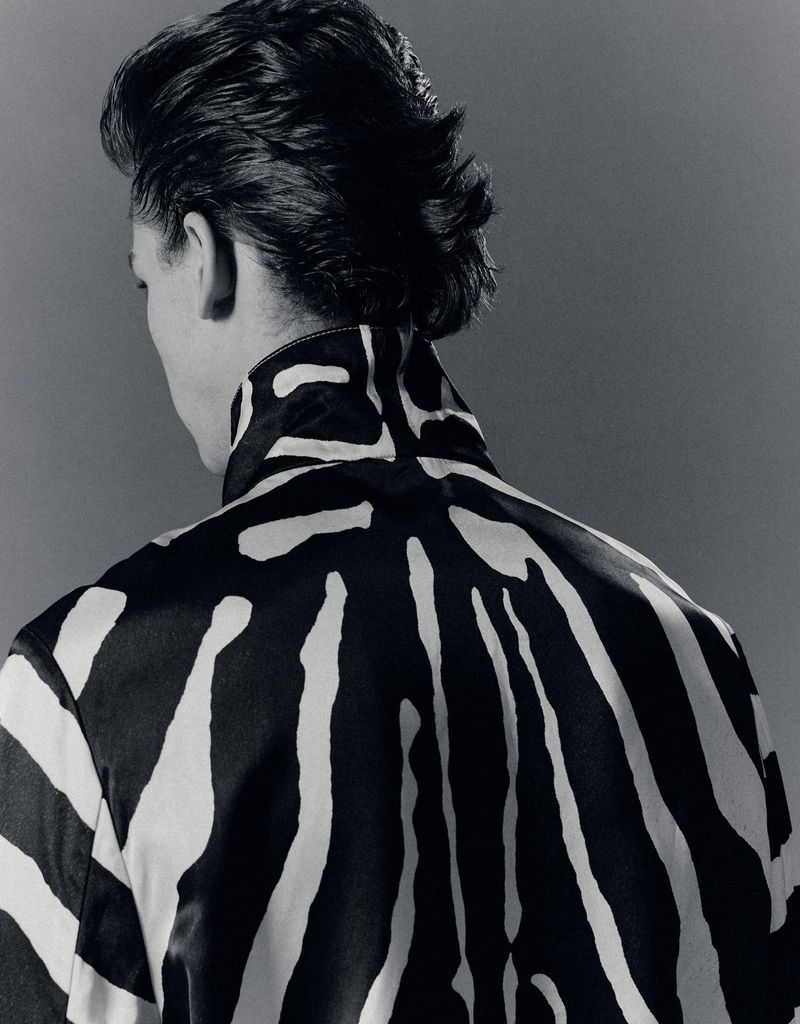 Rear view of a model wearing a black and white patterned jacket against a neutral grey studio backdrop.