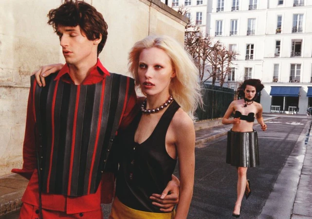 Three models outdoors on a street, featuring a man in a red shirt and a woman with blonde hair in a black top.