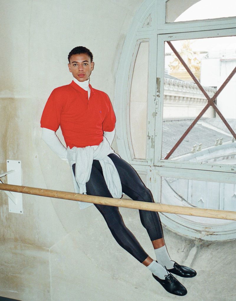 Guillaume Diop in a red polo shirt and dark tights leaning on a ballet barre near a large arched window for El Pais Semanal.