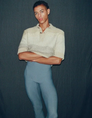 Portrait of Guillaume Diop wearing a cream polo shirt and grey tights against a dark backdrop