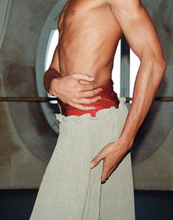 Close-up portrait of shirtless man wearing high-waisted textured trousers and a red fabric sash by Pablo Saez for El Pais Semanal