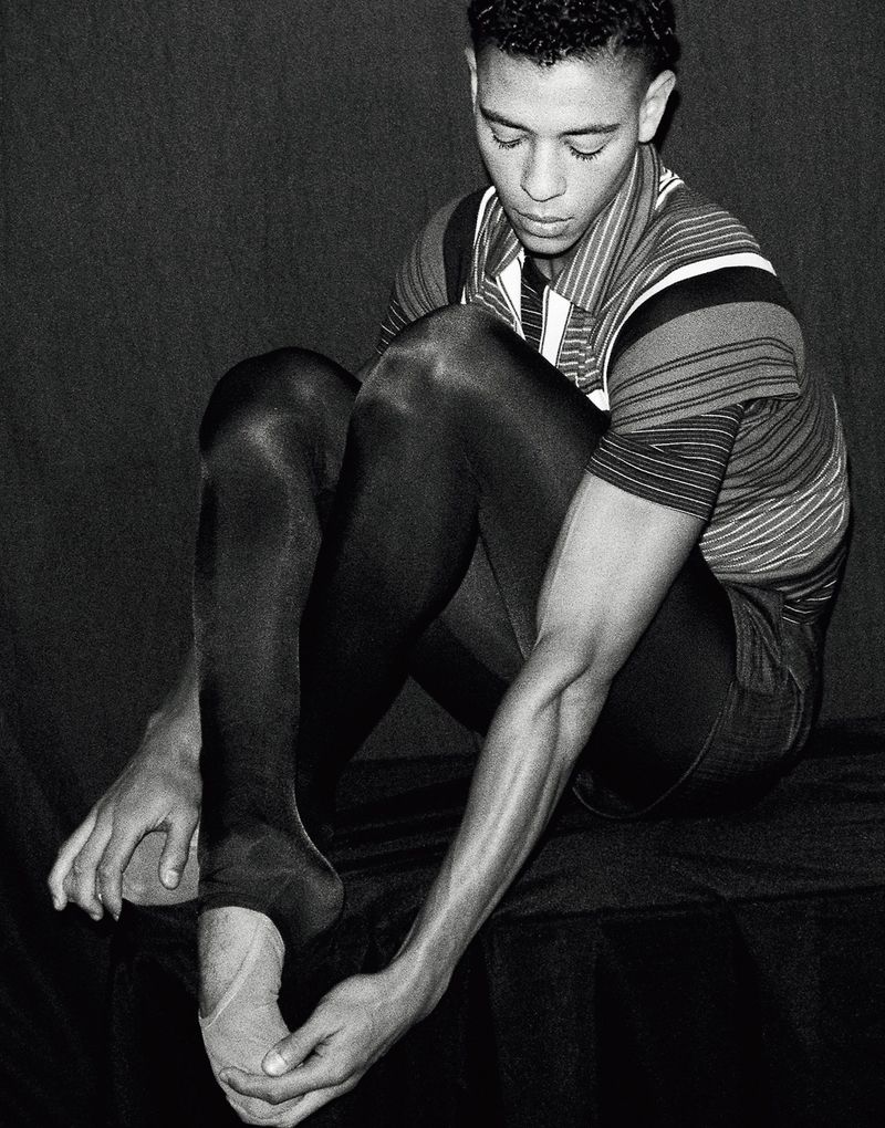 Portrait of dancer Guillaume Diop seated, wearing dark tights and striped polo, captured in black and white for El Pais Semanal.