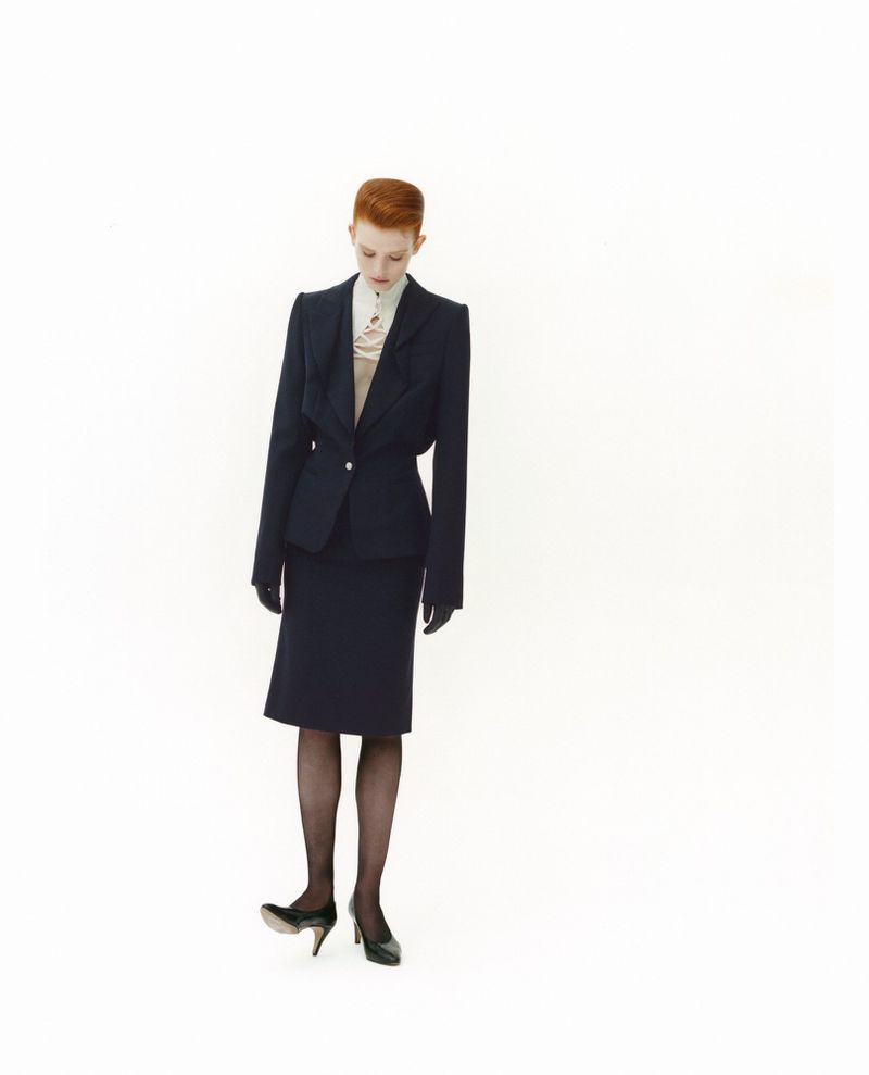 Model with red hair wearing a dark blazer, skirt, and heels against a white seamless background for SSAW Magazine