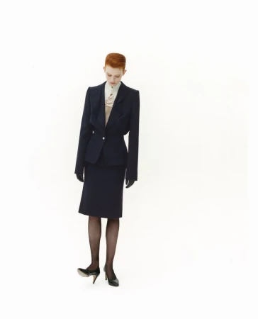Model with red hair wearing a dark blazer, skirt, and heels against a white seamless background for SSAW Magazine