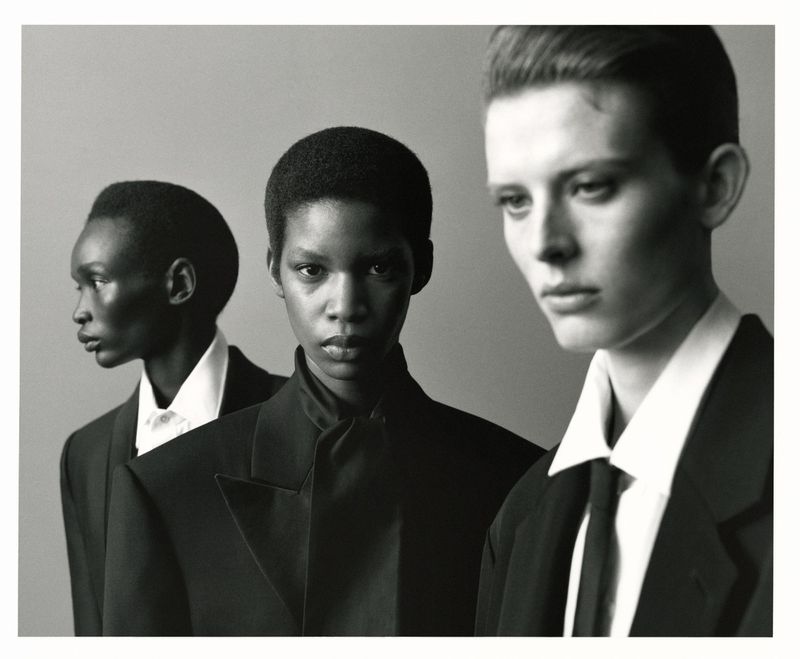 Monochrome fashion portrait of three models in tailored black jackets and white shirts against a plain studio background.