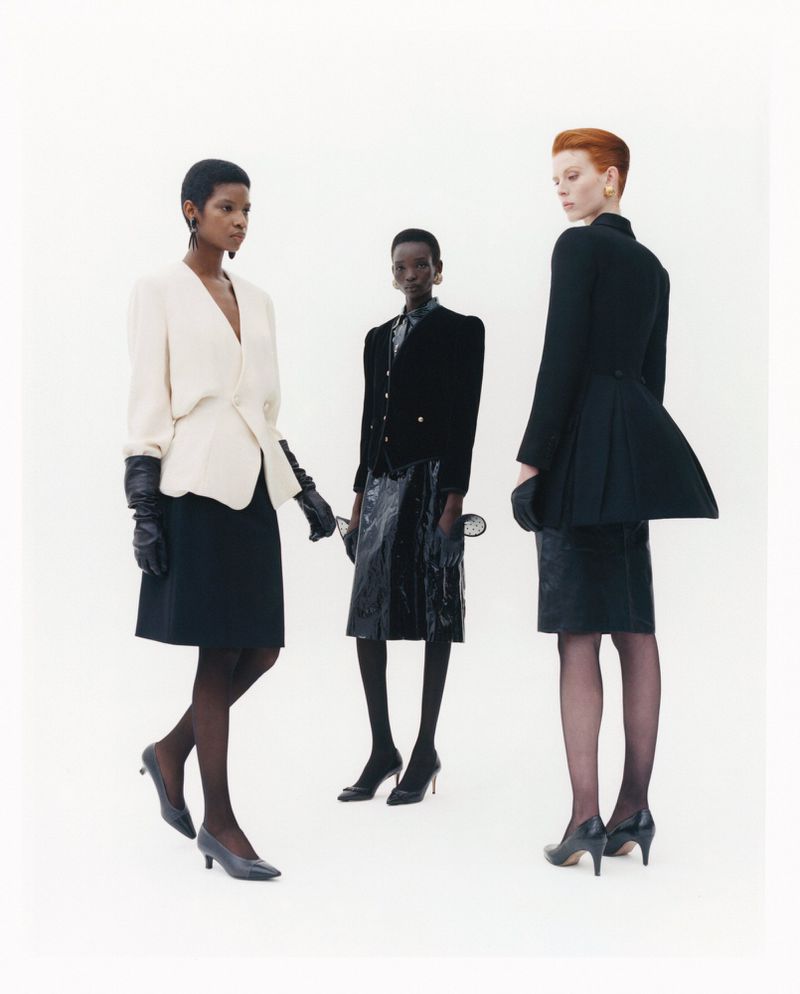 Three models wearing structured jackets and dark skirts against a bright white seamless studio background.