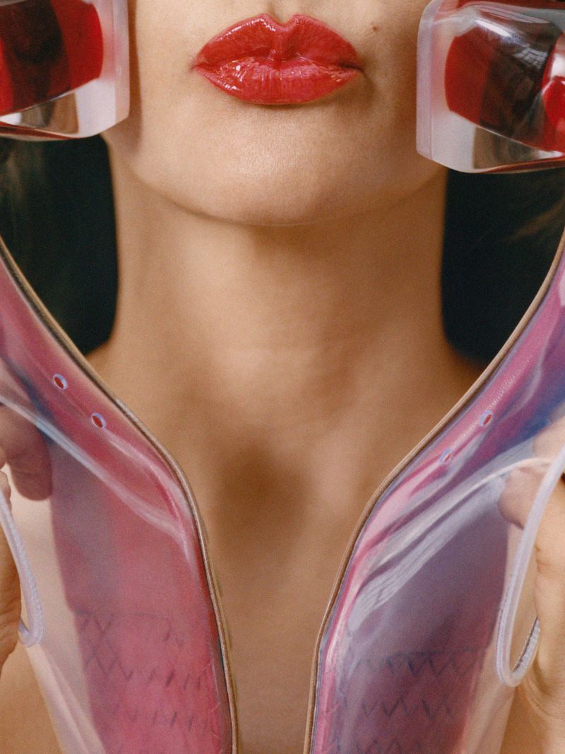 Close-up of woman with glossy red lipstick holding translucent pink sculptural objects near her face