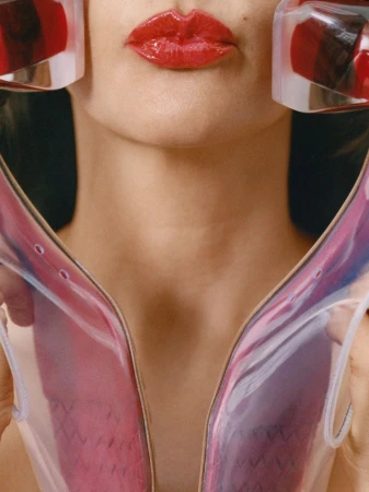 Close-up of woman with glossy red lipstick holding translucent pink sculptural objects near her face