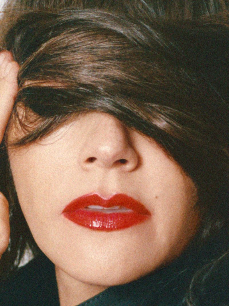 Close-up portrait of Rashida Jones with brown hair partially covering her face and glossy red lipstick for MARFA Good Friends project.