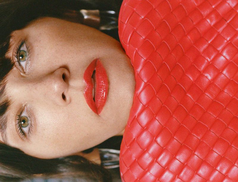 Close-up portrait of Rashida Jones wearing red lipstick beside a bright red woven leather handbag for MARFA Good Friends campaign.