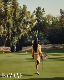 Model wearing a gold textured skirt suit walking away on a green golf course holding a putter, photographed by Vladimir Marti for Harper's Bazaar Arabia