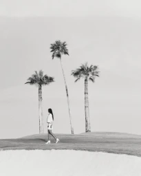 Black and white editorial image of a woman walking past three palm trees on a golf course for Harper's Bazaar Arabia.