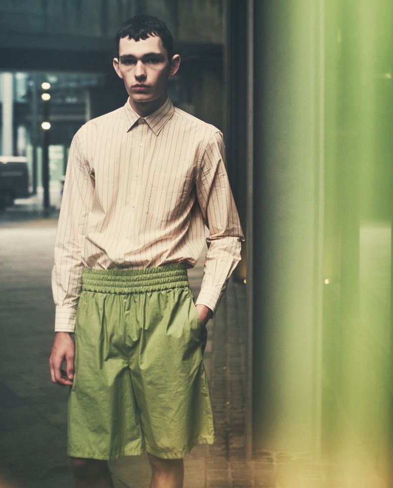 Model wearing a striped button-down shirt and lime green shorts outdoors on an urban street.