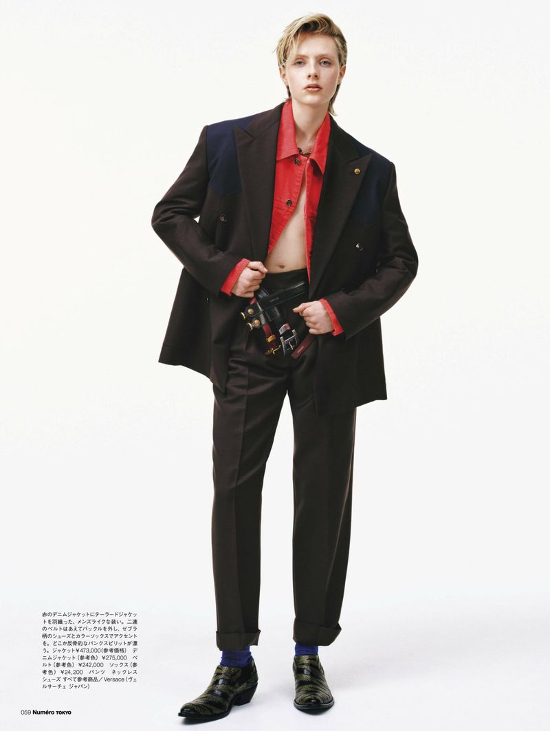 Adult in a fashion editorial posing in a blazer and trousers with a red shirt against a white background, studio lighting, looking at camera.