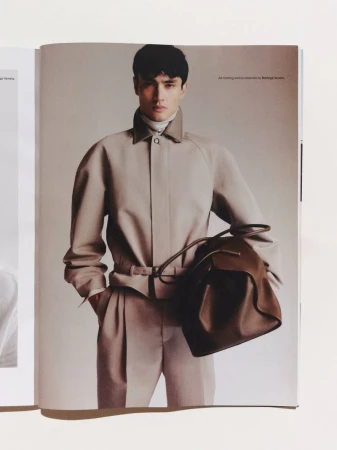 A man in a beige jacket holding a brown leather bag against a neutral studio background for an Esquire Australia editorial.