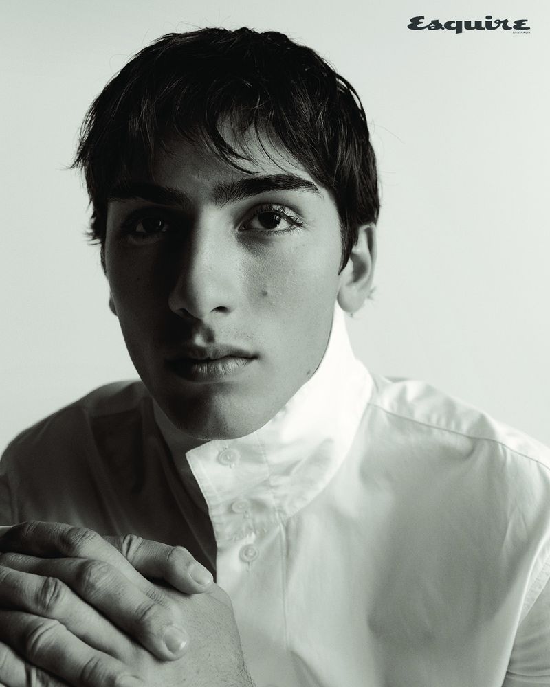 Close-up portrait of a young man with dark hair wearing a white collared shirt against a plain light background