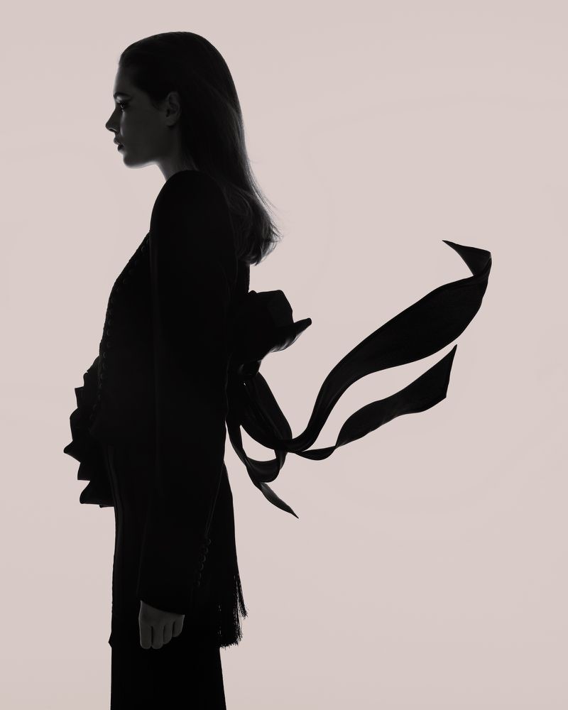Silhouette portrait of a woman in profile against a light background, featuring flowing ribbons attached to her dark garment.