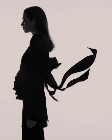 Silhouette portrait of a woman in profile against a light background, featuring flowing ribbons attached to her dark garment.