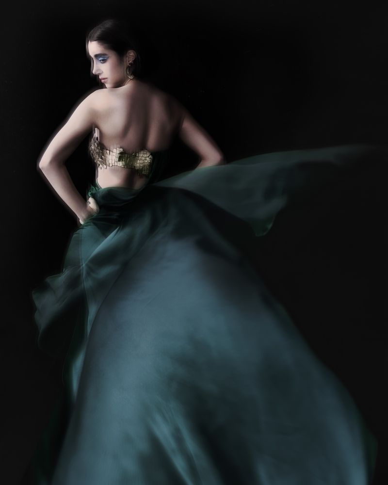 Model in a flowing green gown and metallic corset posing dramatically against a dark background for Numero Netherlands.