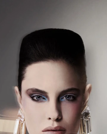 Close-up portrait of a model with voluminous dark hair, blue eyeshadow, and large crystal earrings against a neutral grey background.