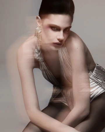 Model in shimmering silver halter top with geometric earrings posing against a neutral grey studio background