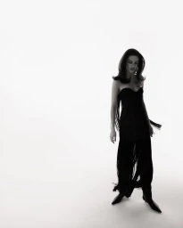 Model in a black fringe dress and boots standing against a bright white studio background.