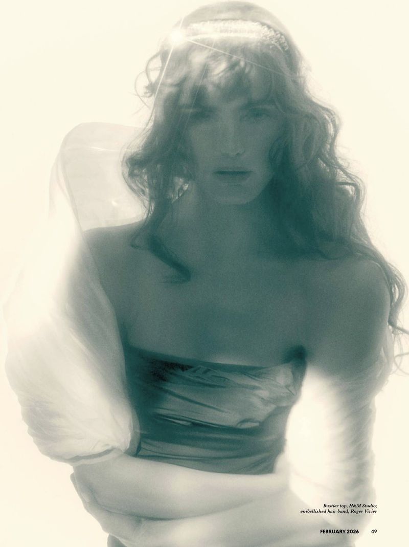 Model with long wavy hair wearing a strapless top and embellished hair band in a soft focus editorial portrait.