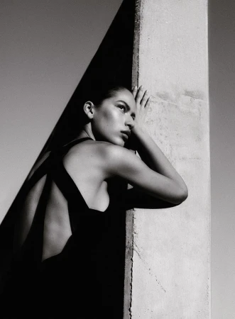 Model in black dress leaning against a concrete pillar outdoors in monochrome editorial fashion portrait