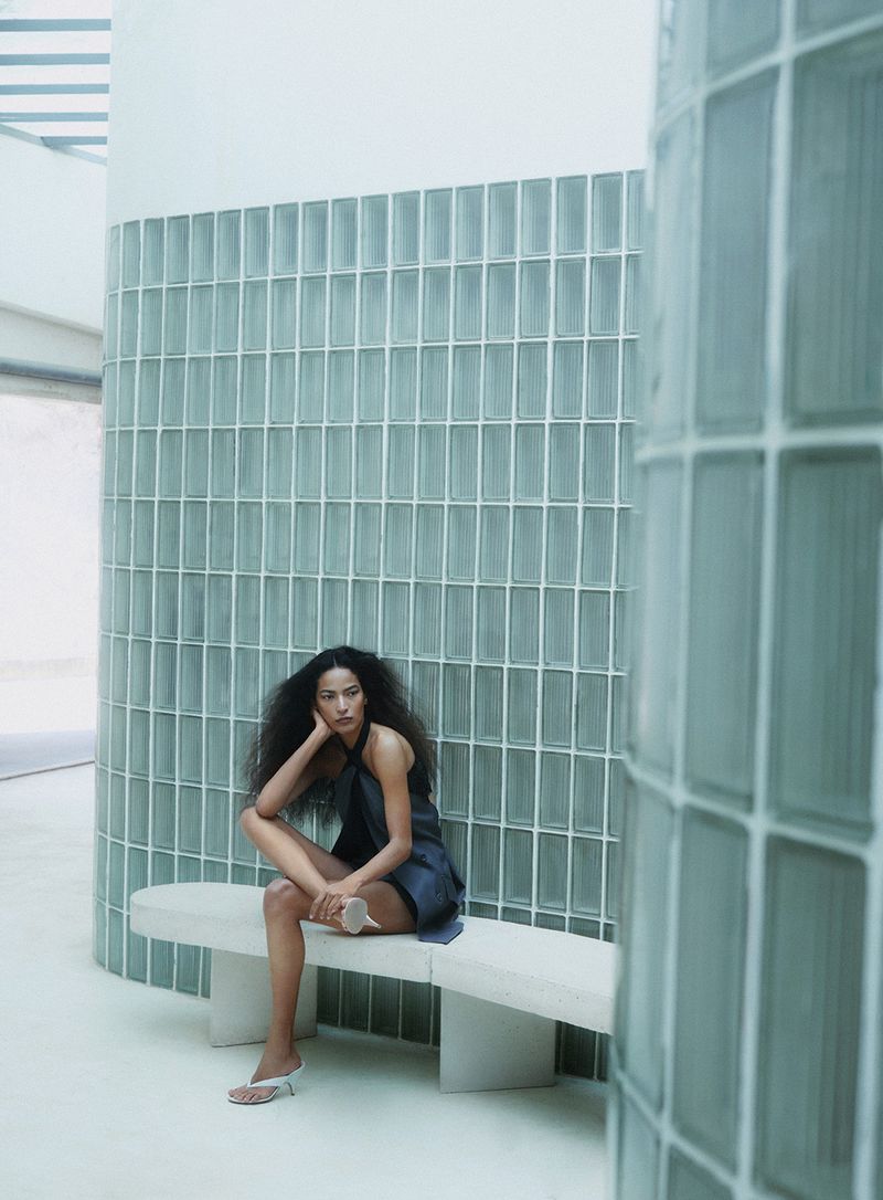 Model with long dark hair seated on a white bench against a curved glass block wall for a Vanity Fair Italia editorial