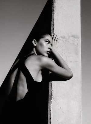 Model in black dress leaning against a concrete pillar outdoors in monochrome editorial fashion portrait