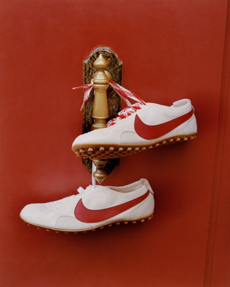 White sneakers with red swoosh hanging from an ornate gold door handle on a red door