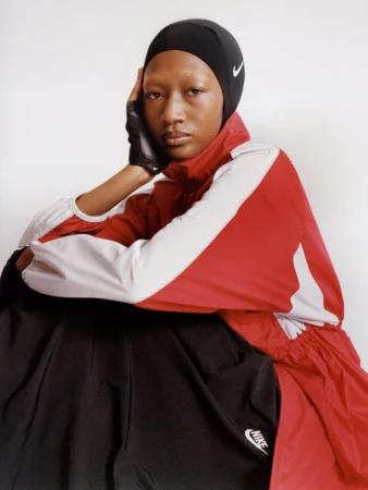 Model wearing a black head covering and red white athletic jacket against a white studio background