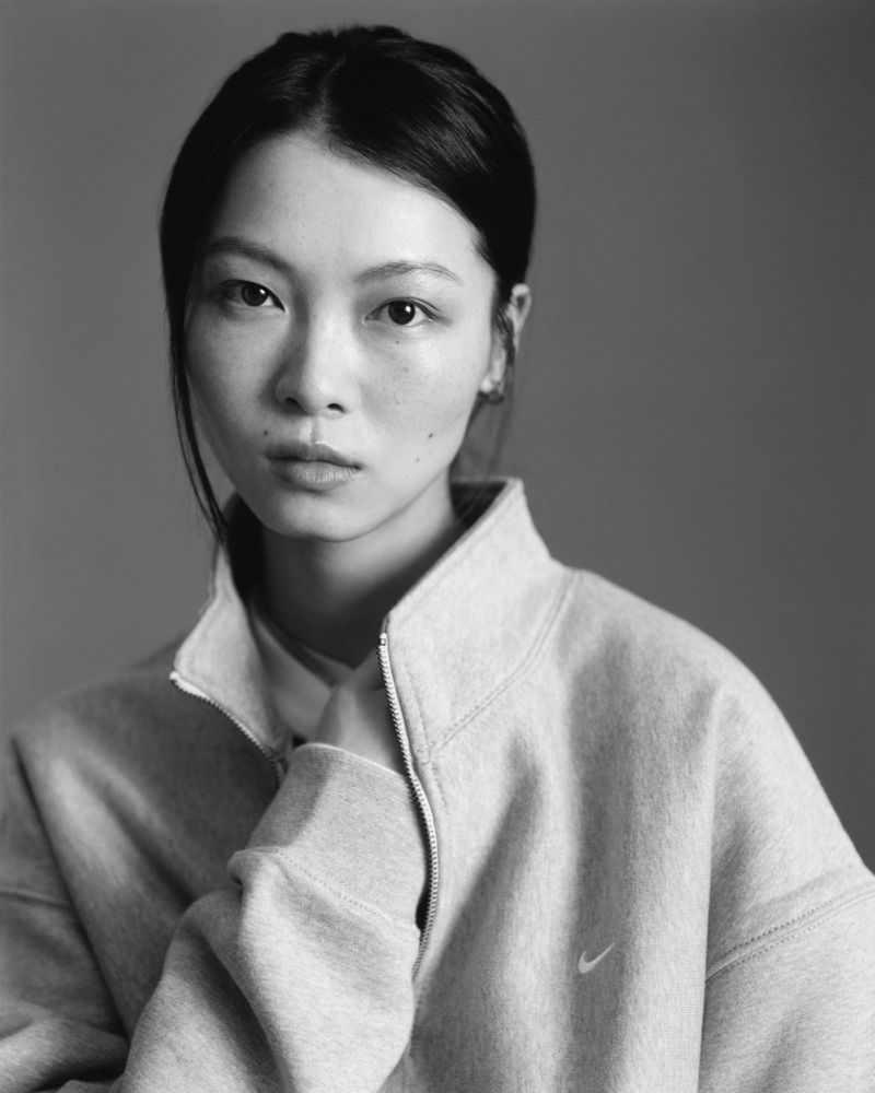 Portrait of a female model wearing a grey zip-up sweatshirt against a neutral grey studio background