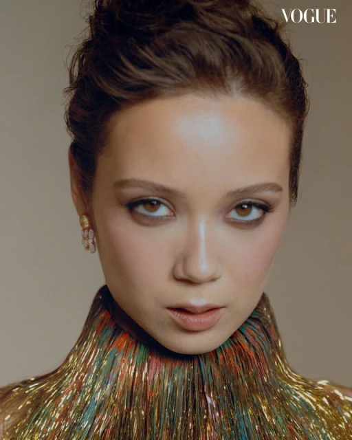 Close-up studio portrait of a young woman with dark hair in a colorful iridescent dress, facing forward with a neutral expression.
