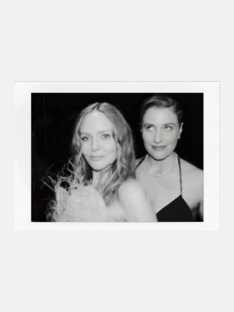 Two women posing together in a monochrome polaroid frame with a dark background.