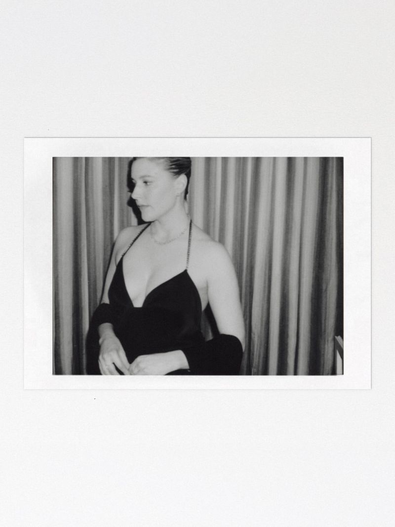 Black and white polaroid photograph of a woman wearing a halter-neck dress against a curtained backdrop.