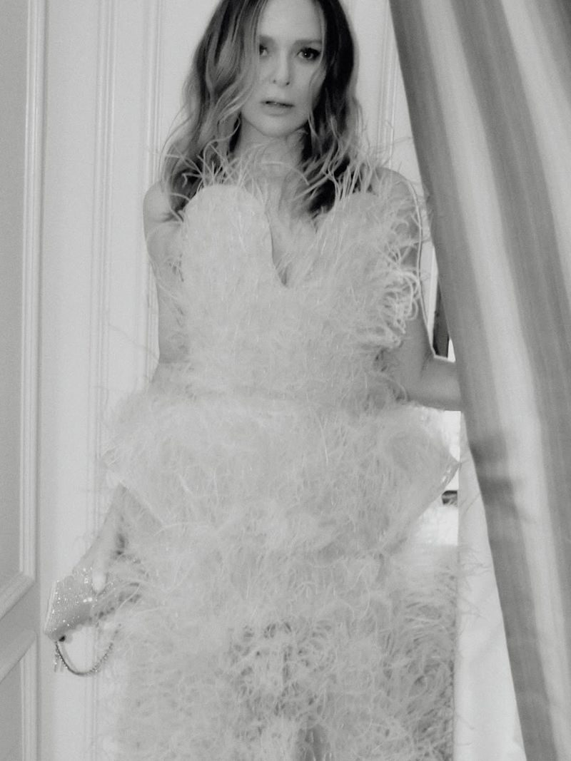 Black and white portrait of a woman wearing a feather-embellished gown holding a small clutch bag indoors.