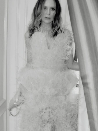 Black and white portrait of a woman wearing a feather-embellished gown holding a small clutch bag indoors.
